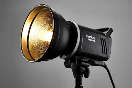 Компактний студійний спалах Godox MS300 зі стандартним рефлектором на стійці, увімкнена лампа моделюючого світла на сірому тлі